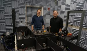 Image of Jens Schmidt and Matthew Comstock stand behind a table on which the optical tweezers sit.